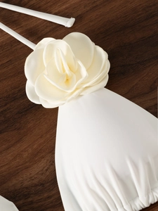 Dettaglio di un top bikini crema decorato con una grande rosa in tessuto 3D satinato