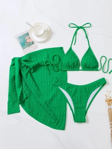 Detailed flat lay of emerald green three-piece bikini set with textured sarong wrap