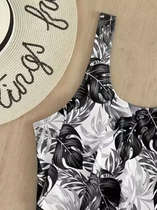 One-piece swimsuit with black and white tropical leaf print on a beach vacation background
