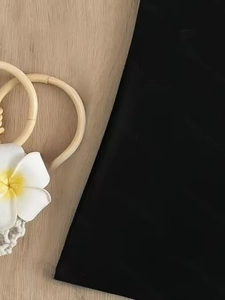 Detailed view of black swimwear fabric on a tropical wooden background with plumeria