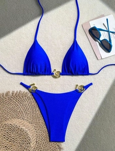 Royal blue two-piece bikini set with golden spiral metal buckles on sand beach props