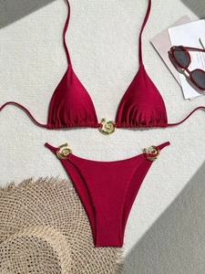 Deep red two-piece bikini set with gold spiral metal buckles on white textured backdrop