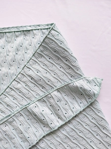 Detail of light blue bikini fabric with wave texture, hollow design, and ruffle edges