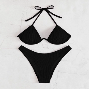Flat lay of black textured halter bikini set with tie-up details on stone surface