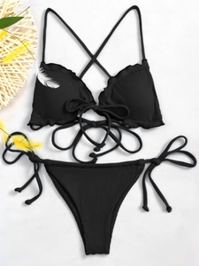 Flat lay of black ribbed bikini with ruffle trim and cross-back straps on white background