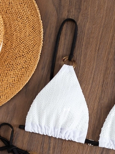 White sequined halter bikini top with tortoiseshell rings on a wooden background
