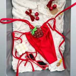 Slip bikini rosso con lacci e fragola di paillettes su uno sfondo di pizzo bianco