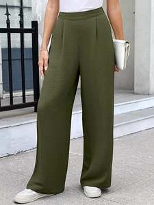 Detail of dark green wide-leg trousers showing waist pleats and textured fabric on model