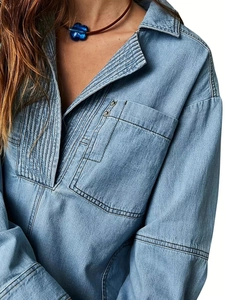 Dettaglio camicia in denim azzurro con pieghe verticali e rivetti metallici decorativi