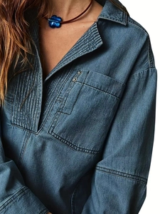 Dettaglio del colletto della camicia di jeans blu scuro con bottoni metallici e collana a fiori