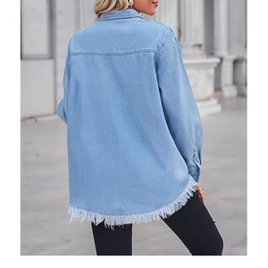 Detail einer hellblauen Jeansbluse mit weißen Fransen am Saum und gewaschenem Denim