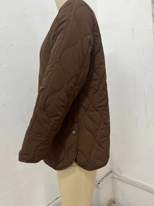Close-up of brown onion-quilted jacket featuring side slits with metallic snap buttons