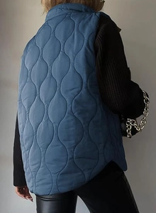 Rear view of a blue quilted vest with a unique wave pattern and high collar design