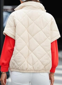 Detail of a quilted cream puffer vest showing diamond stitching and high collar on model