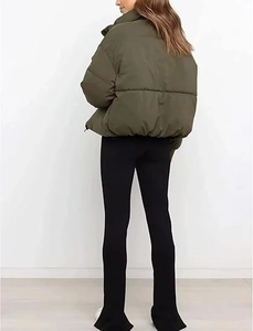Rear view of an olive green puffer jacket with slit-hem black trousers in a studio setting