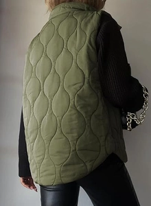Rear view of an olive green quilted puffer vest with wavy stitching and stand collar