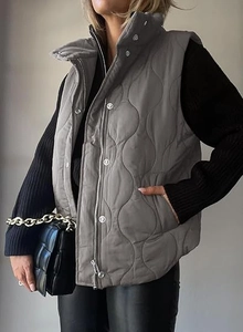 Detail of grey quilted vest featuring wave patterns, zipper closure, and metal buttons