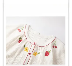 Détail du haut de pyjama en coton blanc avec broderie fraise et boutons rouges contrastés