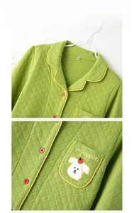 Detail eines grünen gesteppten Pyjama-Oberteils mit Welpenstickerei und roten Knöpfen