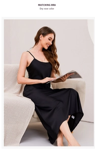 Elegant woman in black silk slip dress sitting on sofa with a magazine in hand