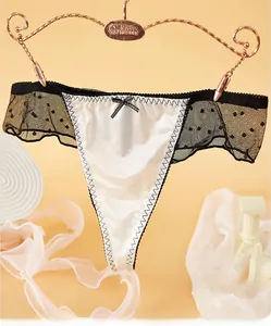 Détail d'un string en satin blanc avec nœud noir et dentelle fine à pois