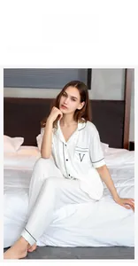 Detail of white modal pajama set with black piping and embroidered pocket on bed