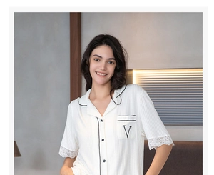 Detail of white modal lounge top featuring black piping, chest pocket V embroidery and lace cuffs