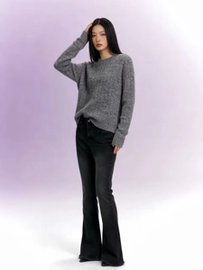 Détail d'un jean évasé noir taille haute porté avec un pull en maille gris et talons