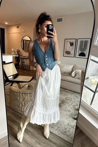 Détail d'un gilet en jean bleu foncé porté avec une jupe bohème blanche à plusieurs niveaux