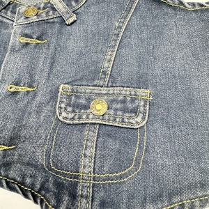 Macro view of vintage denim vest featuring chest pocket detail with metallic jeans button