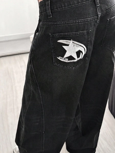 Detail of star embroidery and Beauty text on the back pocket of black washed jeans