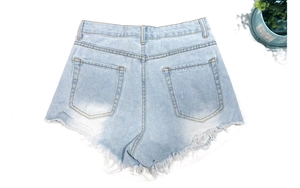 Flat lay of light blue denim shorts with frayed edges and distressed detail texture