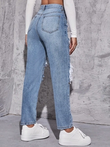 Detail showing distressed fringe rips and light blue washed denim fabric on high waist jeans