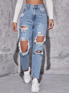 Detailed view of high-waisted distressed light blue jeans with large ripped holes and fringe