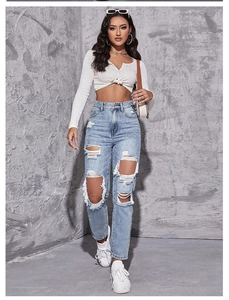 Détail d'un jean droit taille haute avec déchirures et finitions effilochées à franges