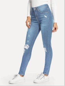Detail of light blue high waist skinny jeans featuring distressed ripped knees and fringe