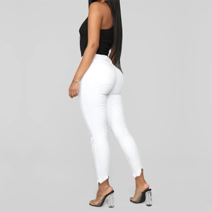 Detail of white high-waisted skinny jeans with ripped knees and raw hem edges