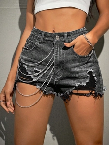 Detail of high-waisted grey denim shorts with distressed holes and side metal chains