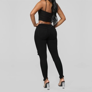 Detail view of high-waist black skinny jeans with frayed hems and distressed side cutouts