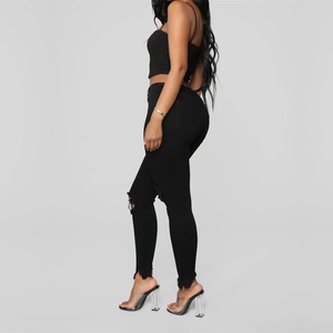 Detail view of black slim-fit distressed jeans with knee rips and frayed hem design