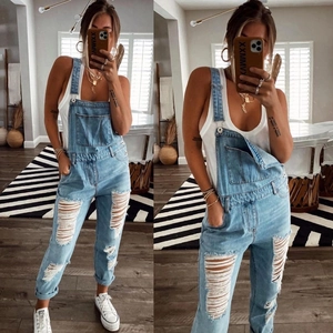 Detailed view of light blue distressed denim overalls with trendy ripped knees and rolled cuffs