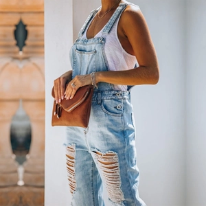 Detail shot of distressed light blue denim overalls with ripped holes and metal buttons