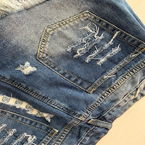 Détail de short en jean avec imprimé étoile, poches usées et surpiqûres jaunes vives