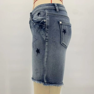 Detail view of denim shorts featuring star embroidery and raw hem design on the side