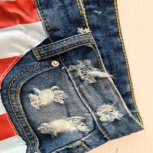 Détail d'un short en jean bleu délavé montrant des trous effilochés et des accents rayés rouge et blanc