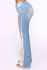 Detail of light blue flared jeans showing side distressing and white fringe tassels