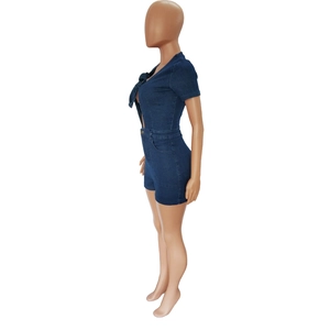 Side view of dark blue denim romper featuring short sleeves and front bow tie detail