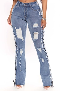 Detailed view of blue distressed jeans featuring side lace-up eyelets and frayed edges