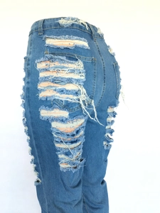 Détail d'un jean bleu taille haute avec de larges déchirures et des franges sur la hanche