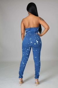 Detail of slim fit strapless denim jumpsuit featuring white paint splatter and back zipper